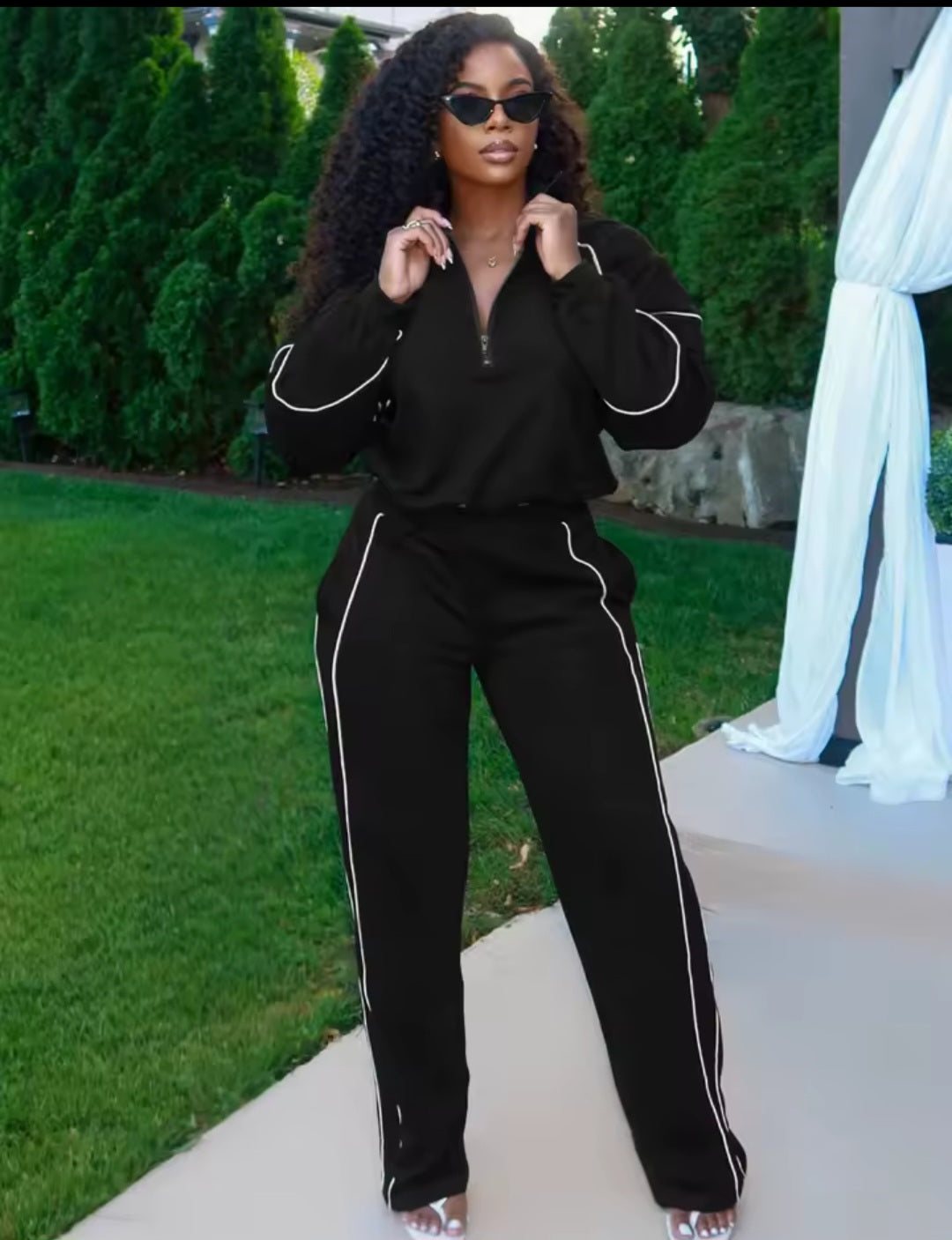 Woman in a black tracksuit with white stripes standing outdoors.