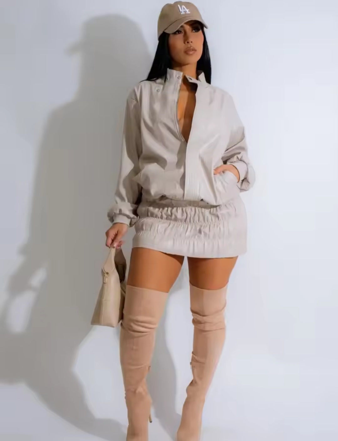 Woman wearing a beige outfit with over-the-knee boots against a white background