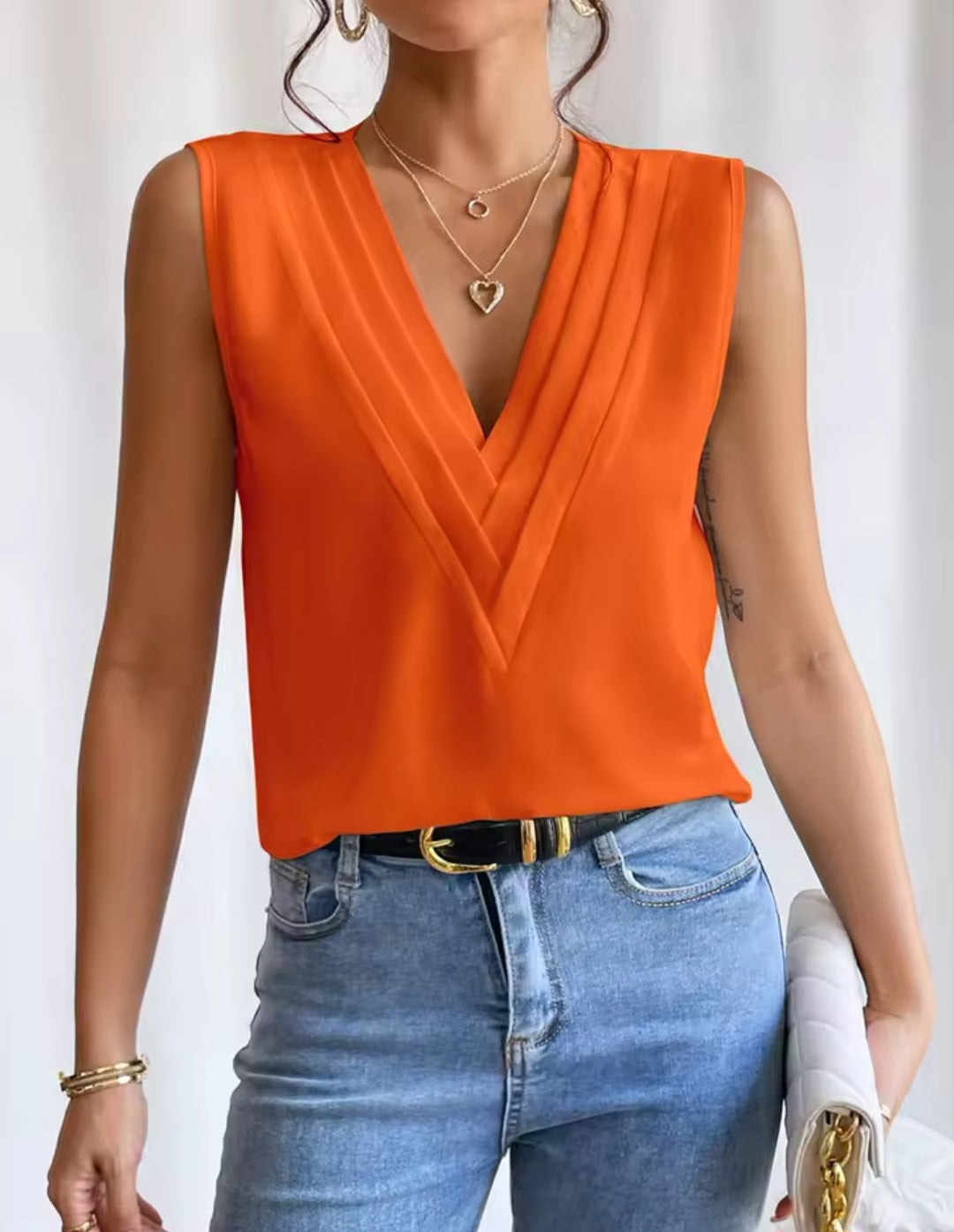 Person wearing an orange sleeveless top and blue jeans against a white background