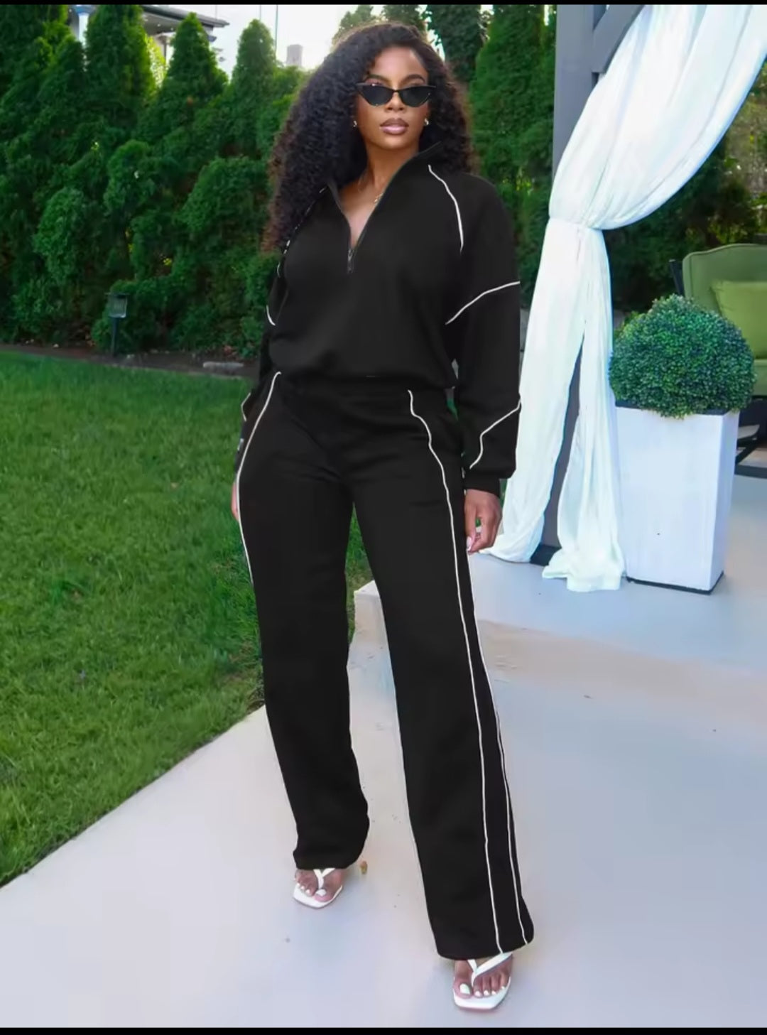 Woman wearing a black outfit with white piping in an outdoor setting.