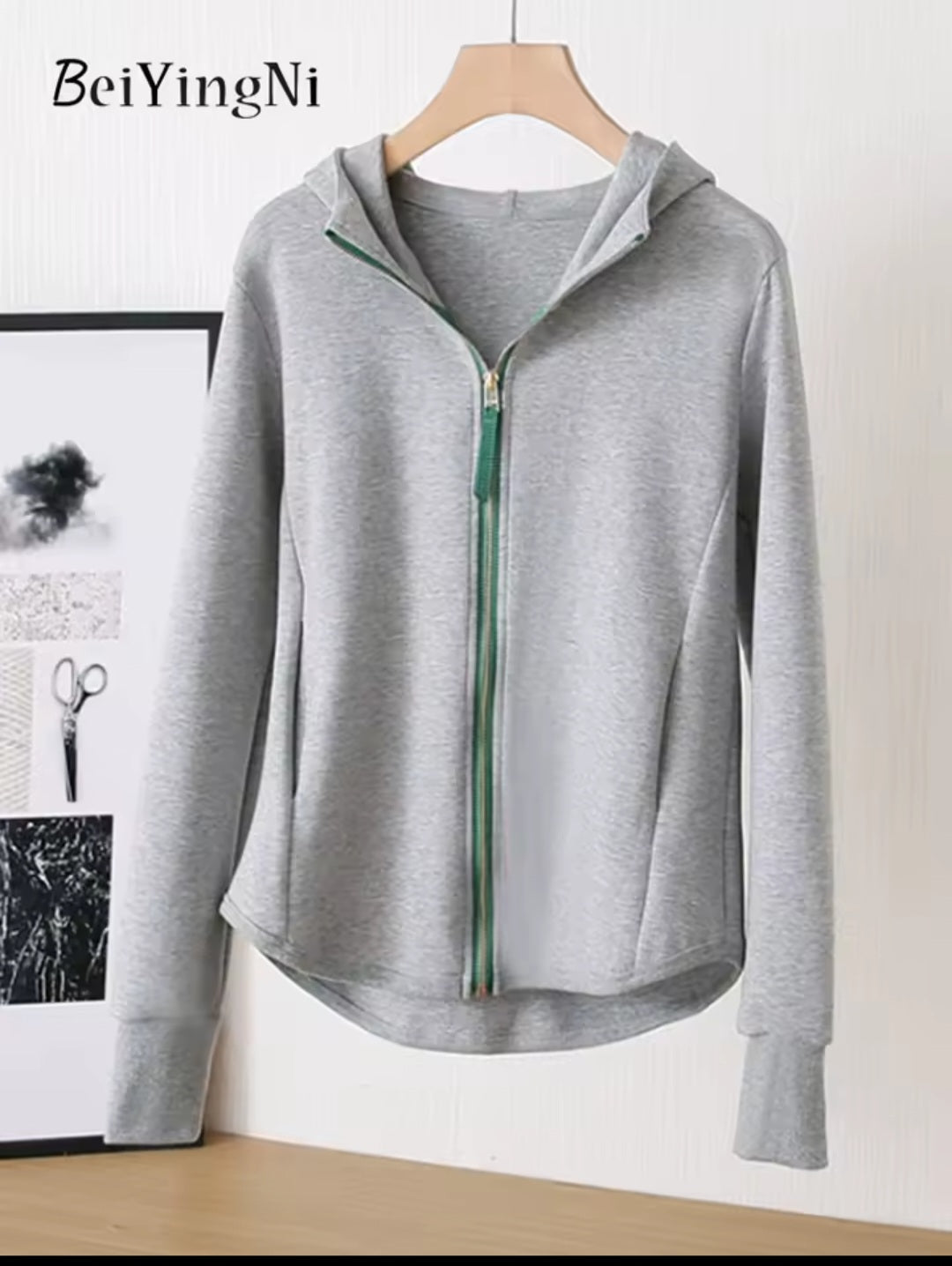 Gray hoodie with a green zipper on a hanger against a white wall.