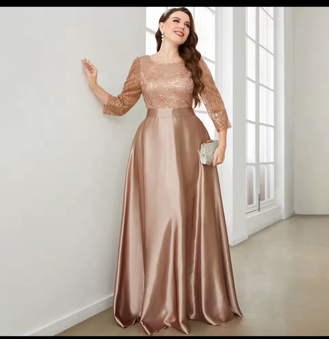 Woman in a rose gold evening gown standing in a room with large windows.
