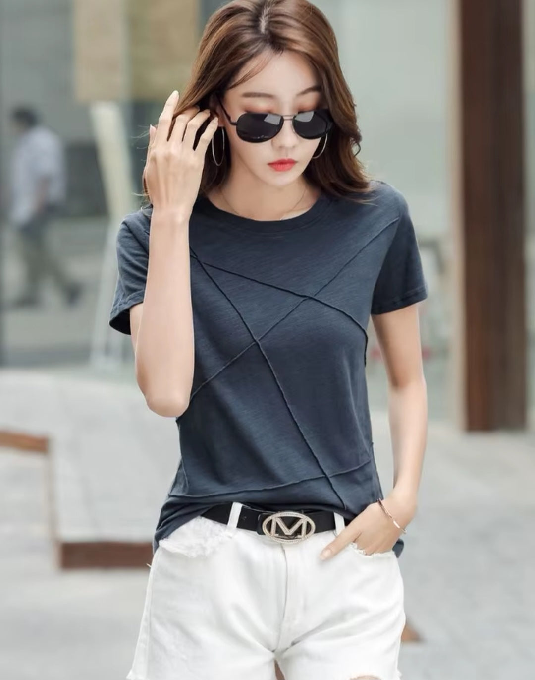 Woman wearing a dark blue top and white pants with sunglasses, standing outdoors.