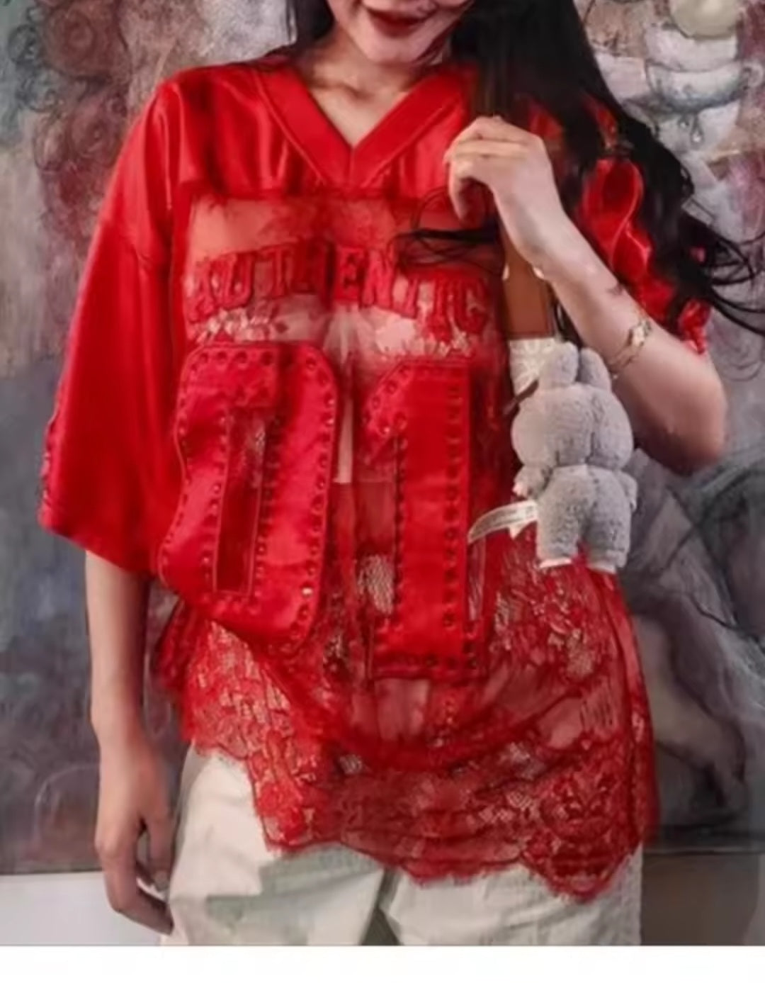 Person wearing a red oversized shirt with text, holding a red bag.