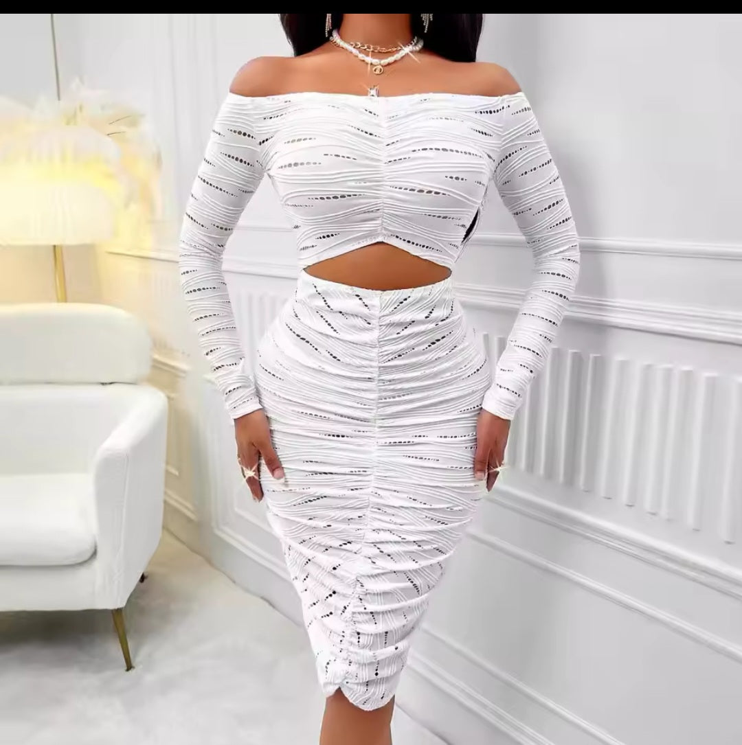 Woman wearing a white off-shoulder outfit in a room with a white armchair and lamp.