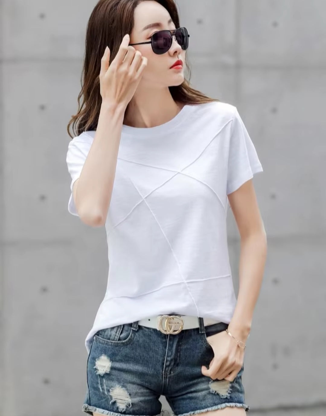 Woman wearing a white t-shirt and denim shorts against a gray concrete wall.