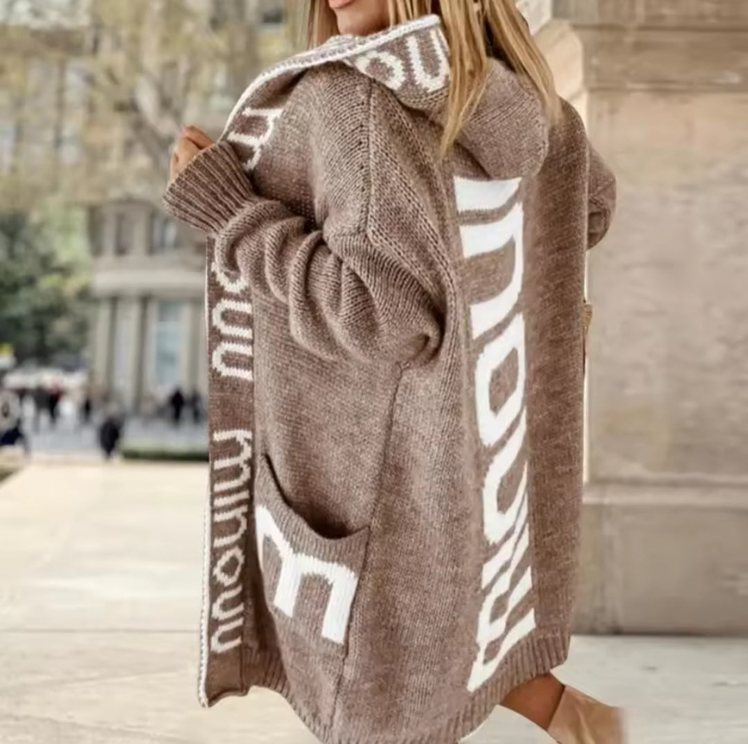 Person wearing a brown cardigan with white text outdoors