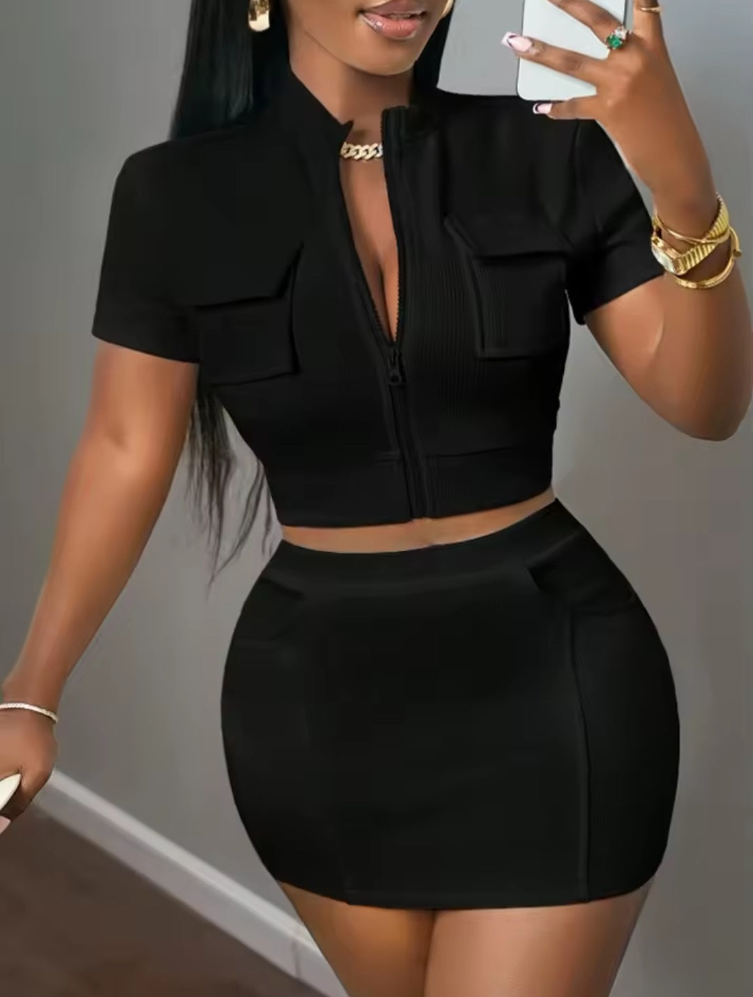 Woman wearing a black outfit taking a mirror selfie against a gray background