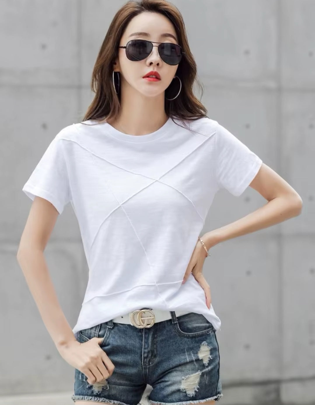 Woman wearing a white t-shirt and denim shorts with sunglasses against a gray background