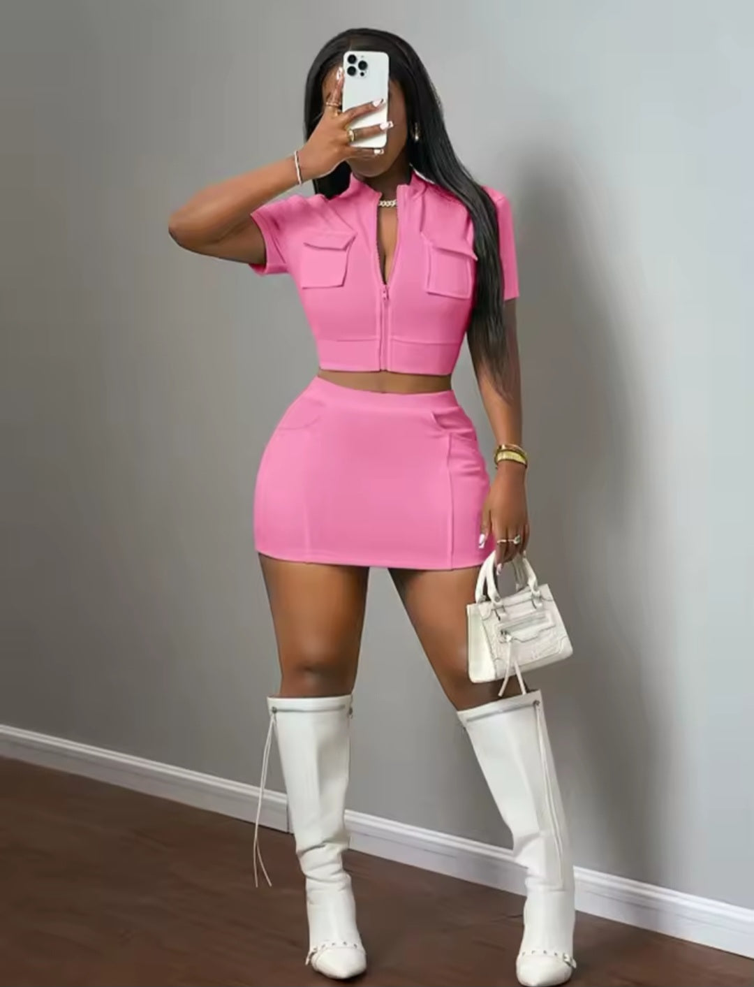 Person wearing a pink outfit with a skirt and top, standing against a gray wall.