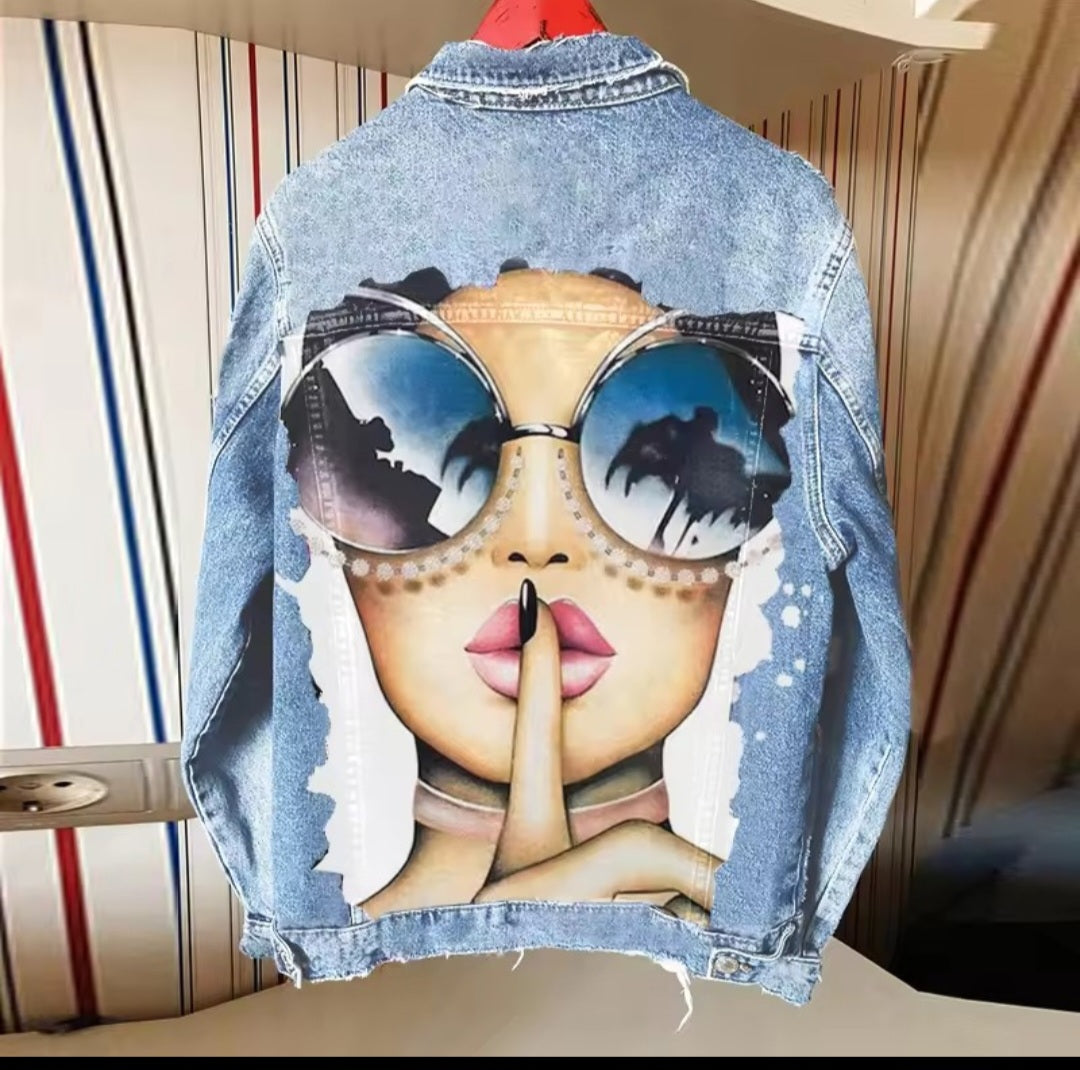 Denim jacket with a graphic design of a face wearing sunglasses and a 'shh' gesture.