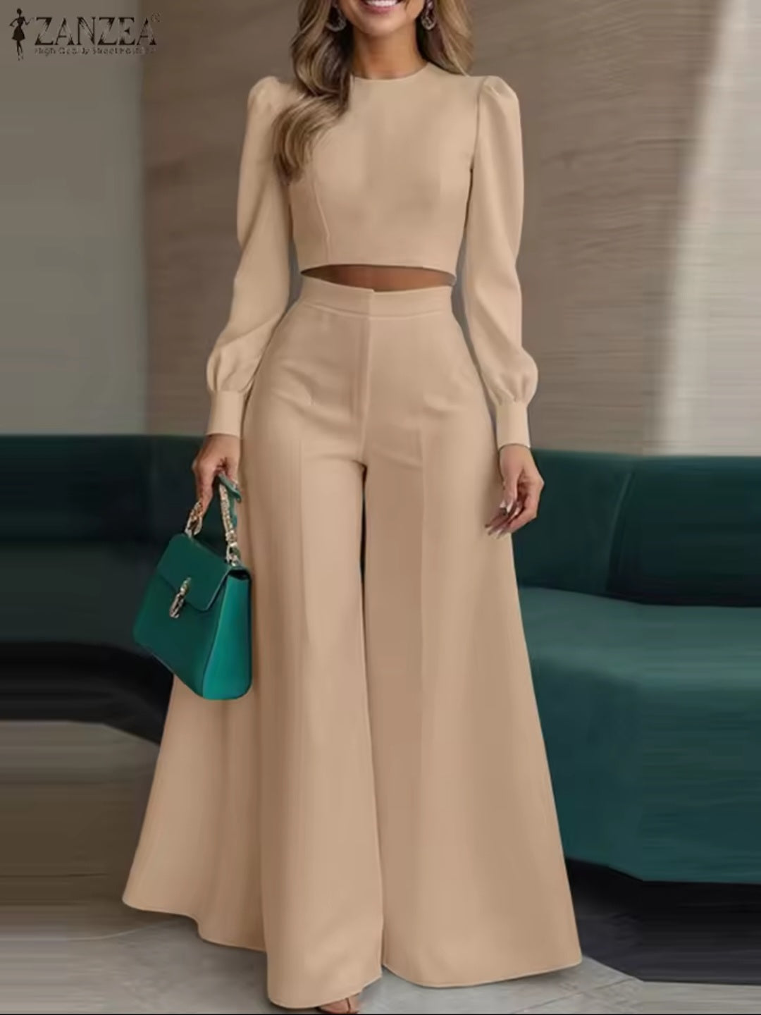Woman wearing a beige outfit holding a green handbag in an indoor setting.