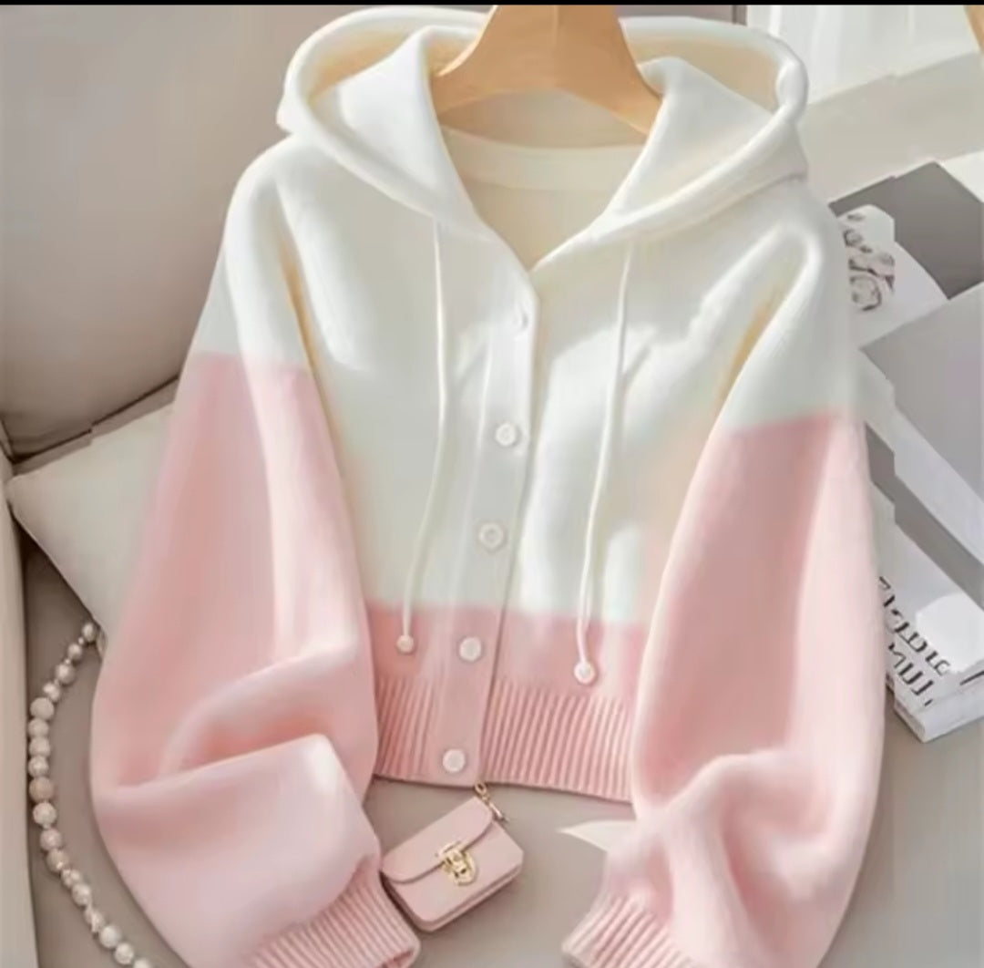 White and pink gradient cardigan on a hanger with a small handbag and books in the background.
