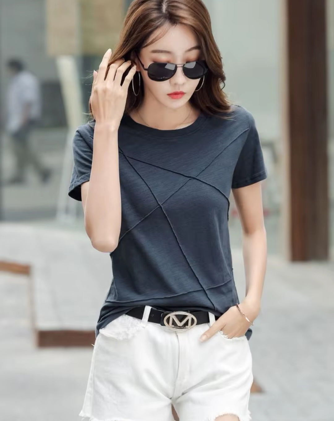 Woman wearing a dark gray top and white shorts with sunglasses, standing outdoors.