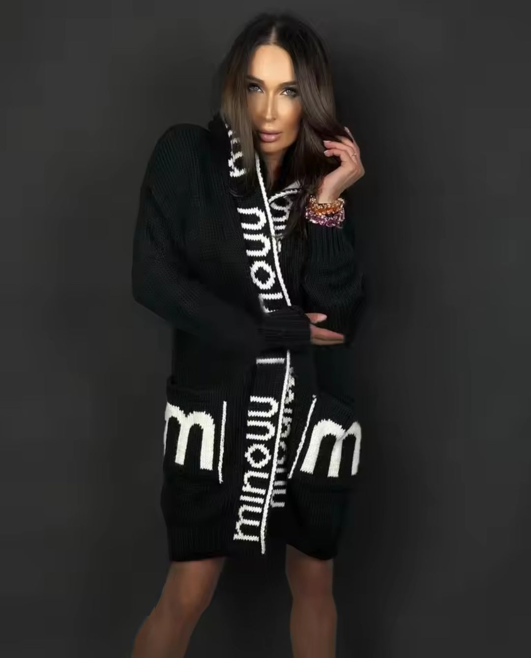 Woman wearing a black cardigan with white branding against a dark background