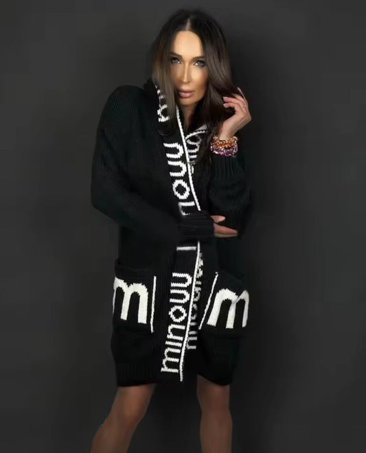 Woman wearing a black cardigan with white branding against a dark background