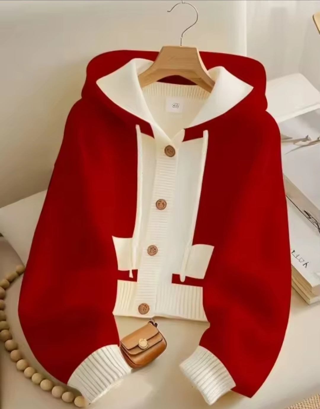 Red and white cardigan with buttons on a hanger against a neutral background
