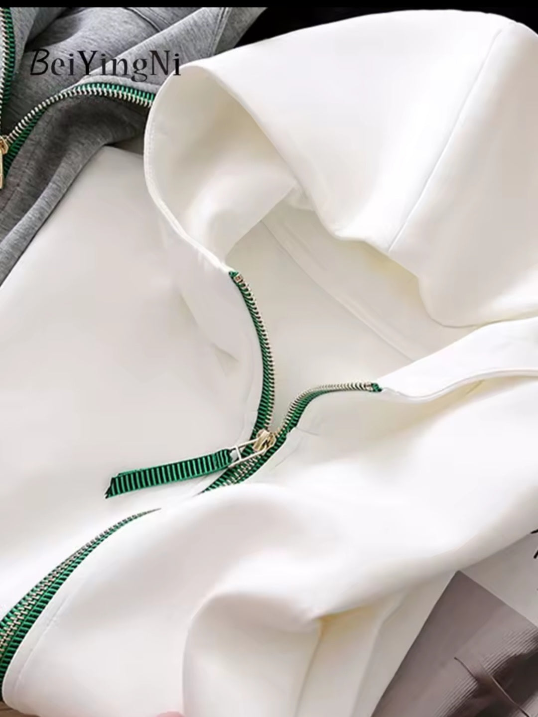 Close-up of a white garment with green zipper details, brand 'BeiYingNi' visible.