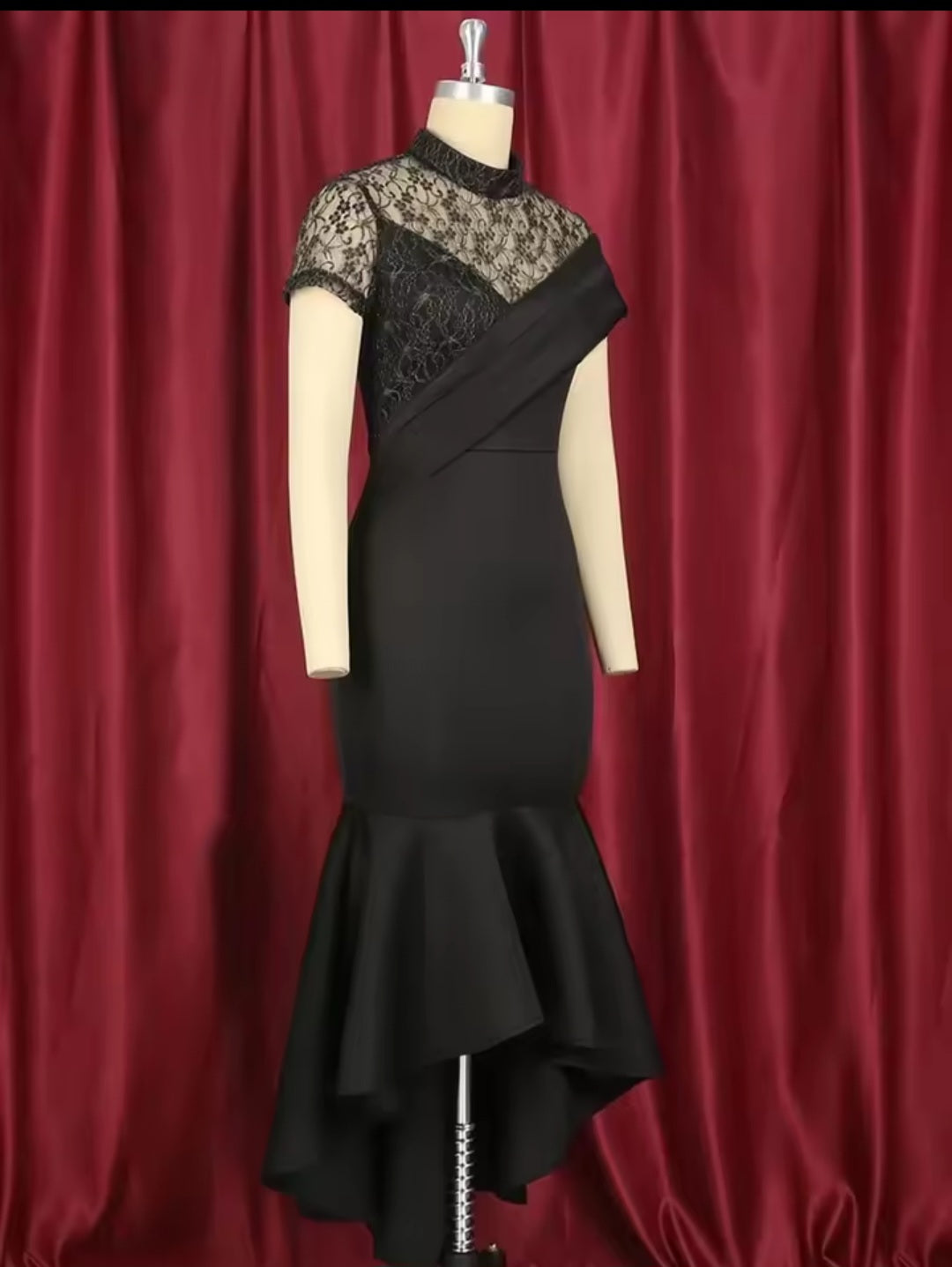 Black dress with lace detailing on a mannequin against a red curtain background