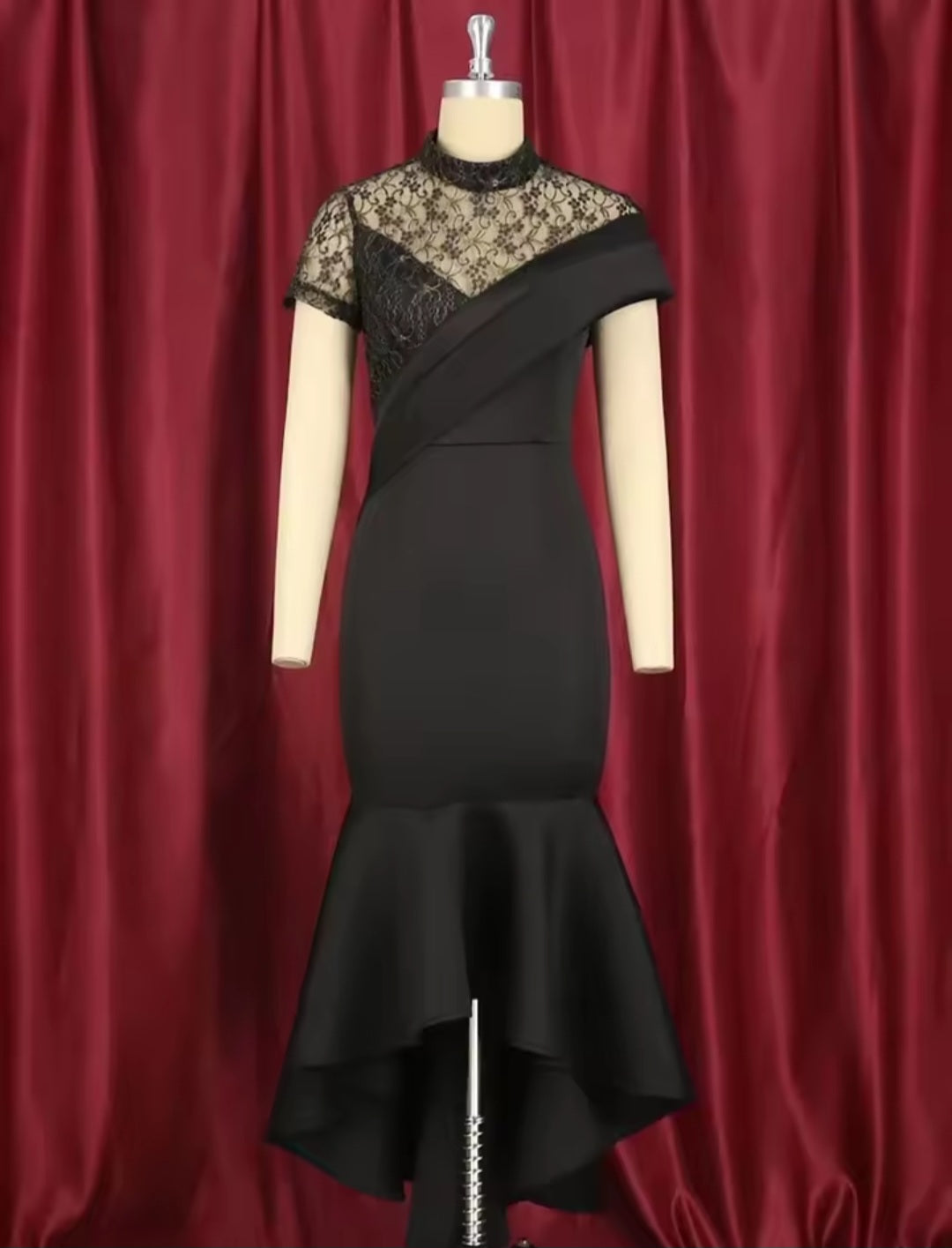 Black dress with floral lace details on a mannequin against a red curtain background