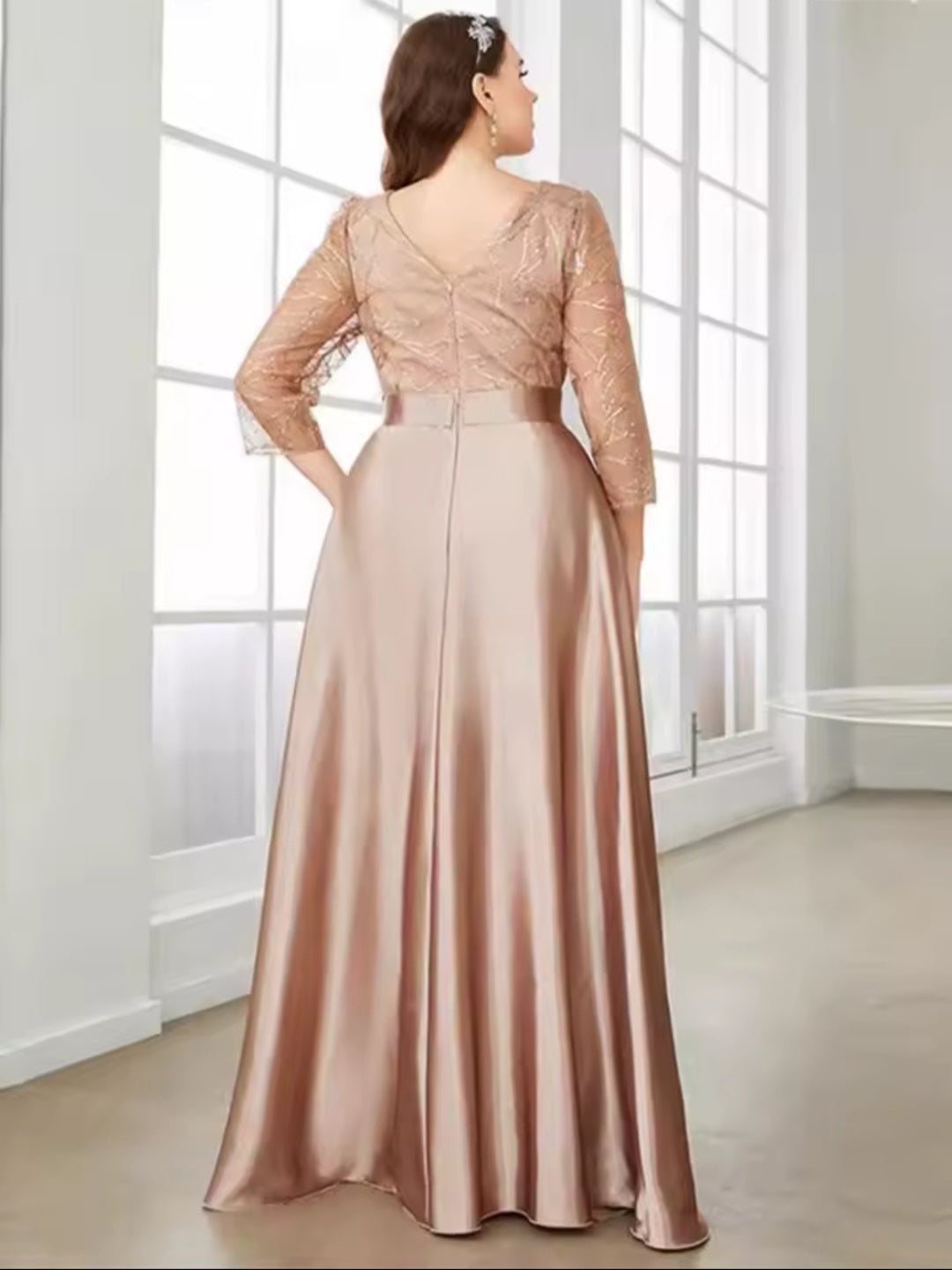 Woman wearing a long, elegant dress with lace top and satin skirt in a bright room.