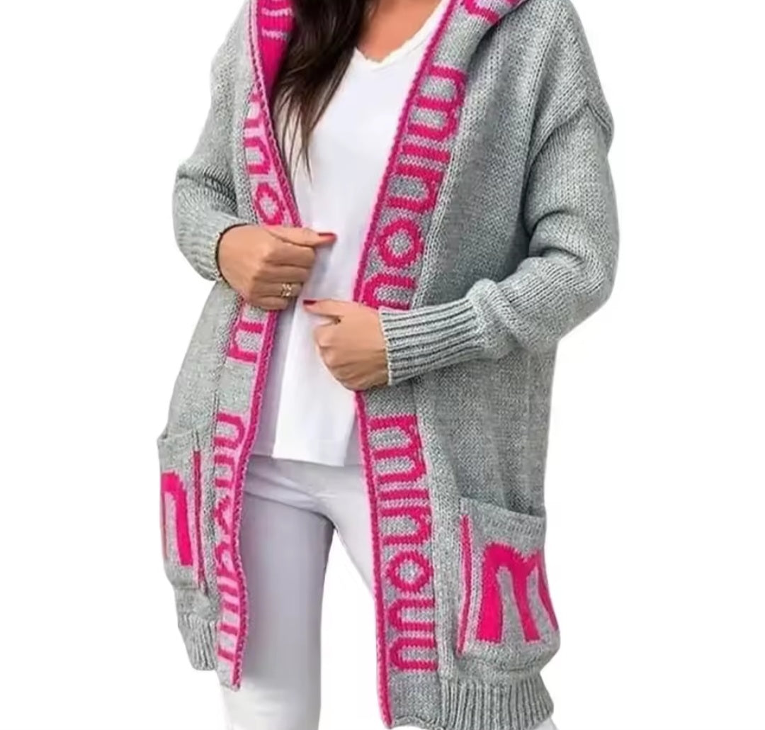 Gray cardigan with pink lettering worn by a person on a white background