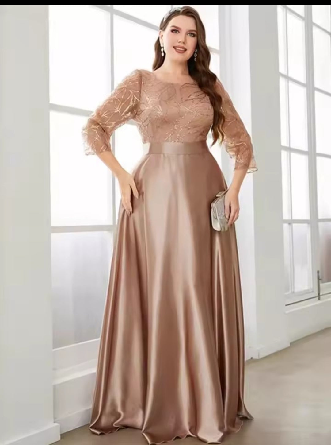 Woman wearing a long, elegant dress with sheer sleeves in a bright room.