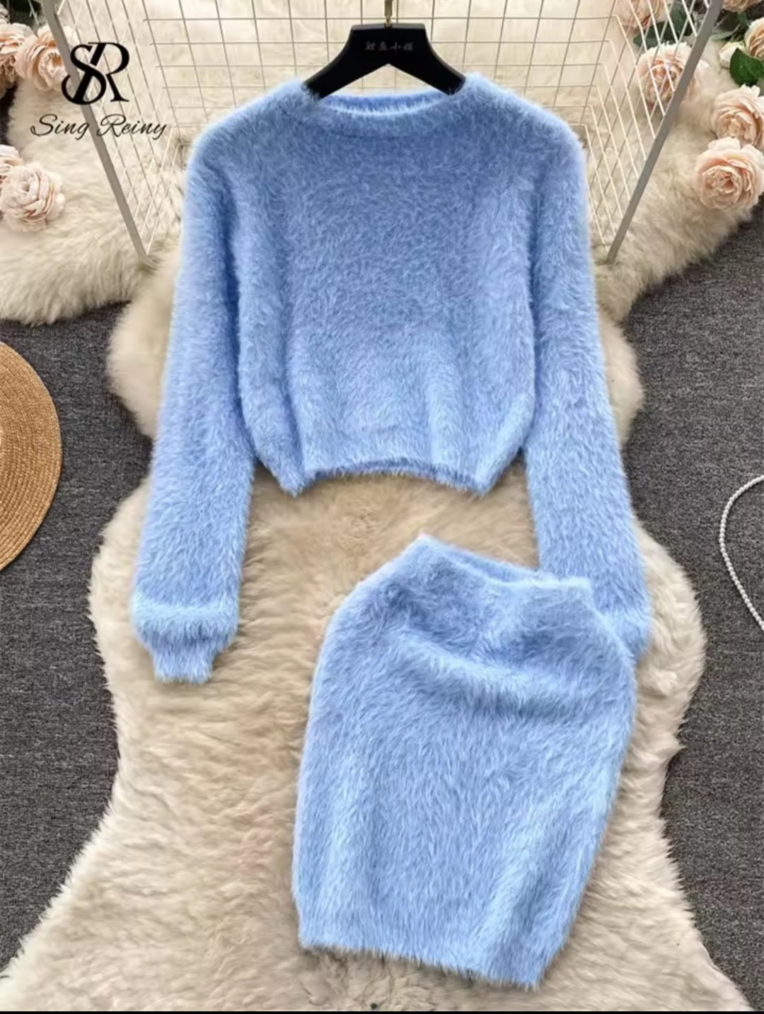 Light blue fuzzy sweater and skirt set on a hanger with flowers in the background