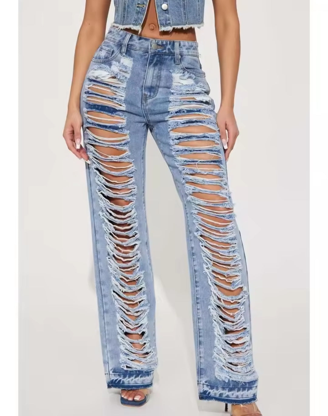 Ripped blue jeans worn by a person on a white background