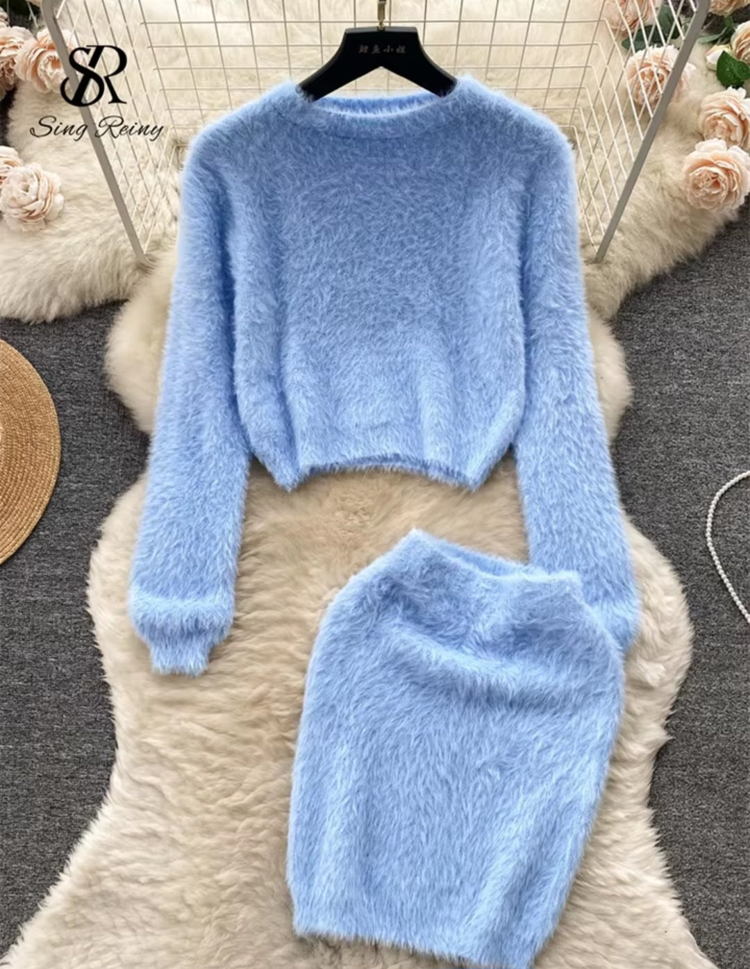 Light blue fuzzy sweater and pants set on a textured surface with flowers in the background.
