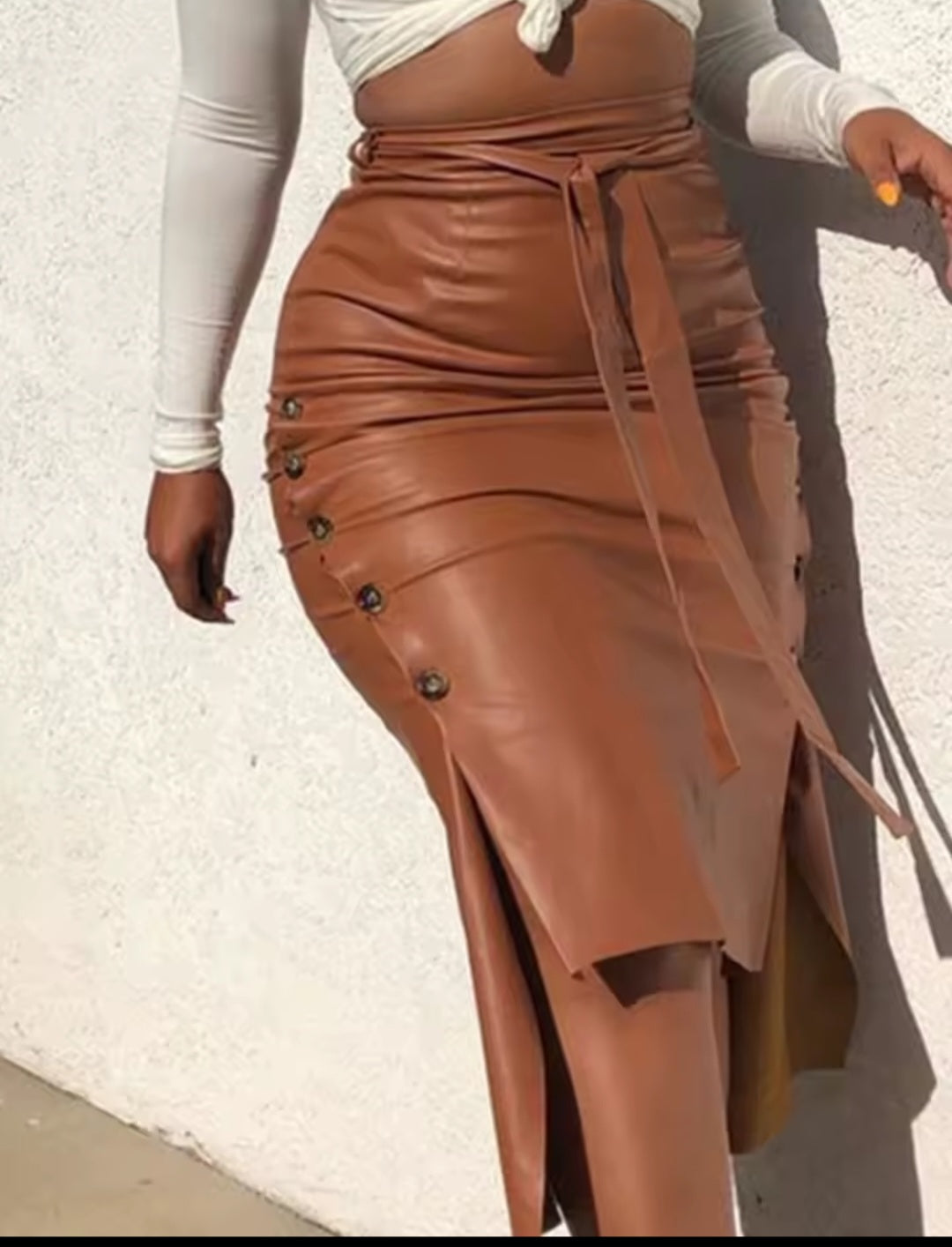 Brown leather skirt with button details worn by a person against a white wall.