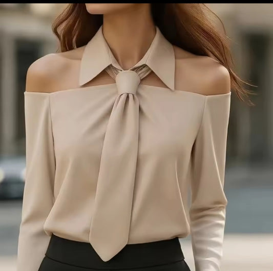Beige off-shoulder blouse with a large bow detail on a blurred street background