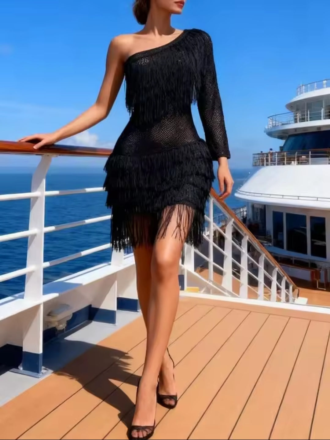 Woman in a black one-shoulder dress with fringe standing on a cruise ship deck.
