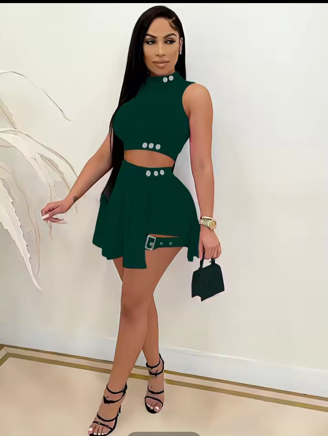 Woman in a green dress holding a black handbag indoors.