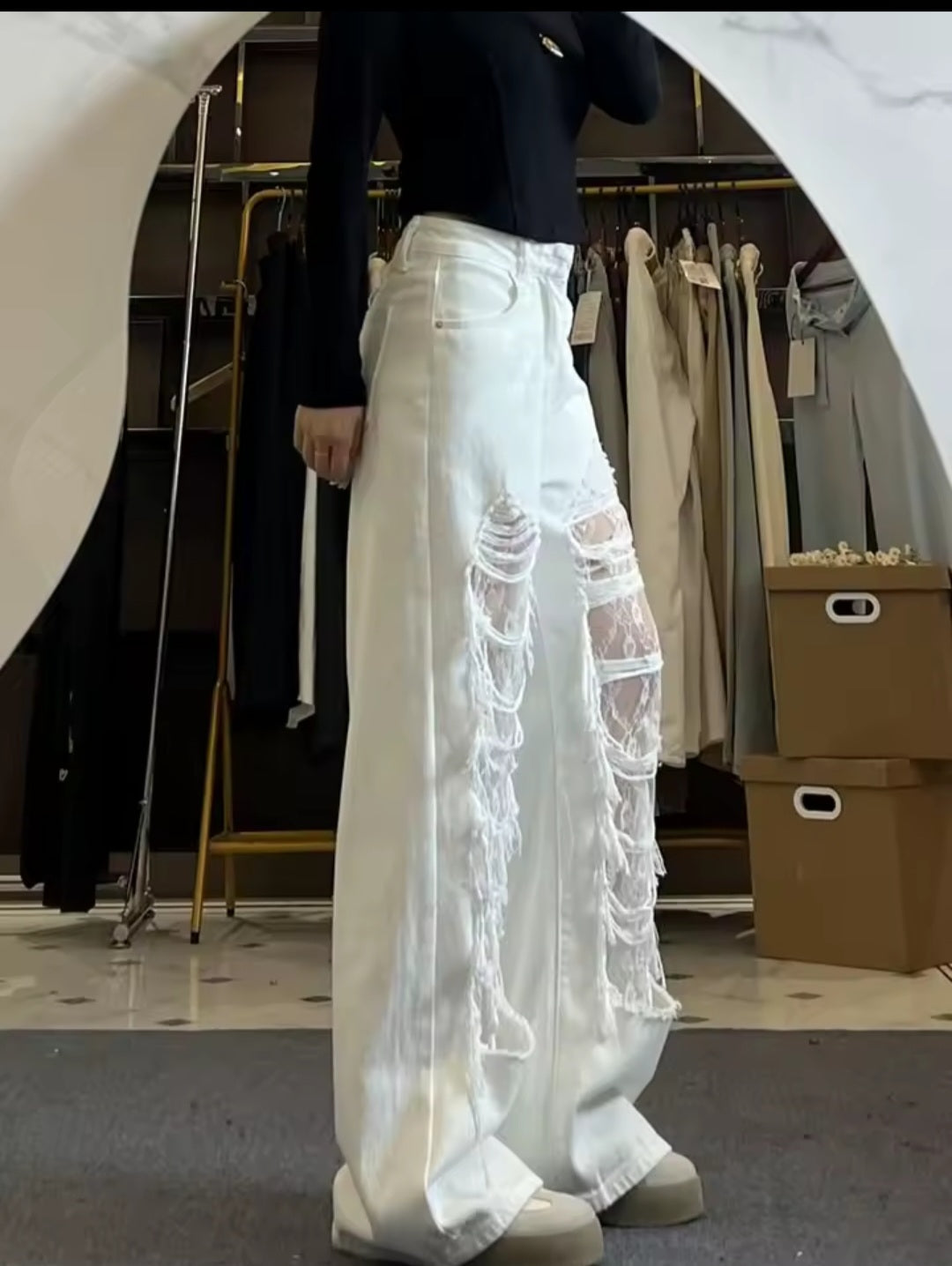 Person wearing white pants with sheer lace detailing in a clothing store.