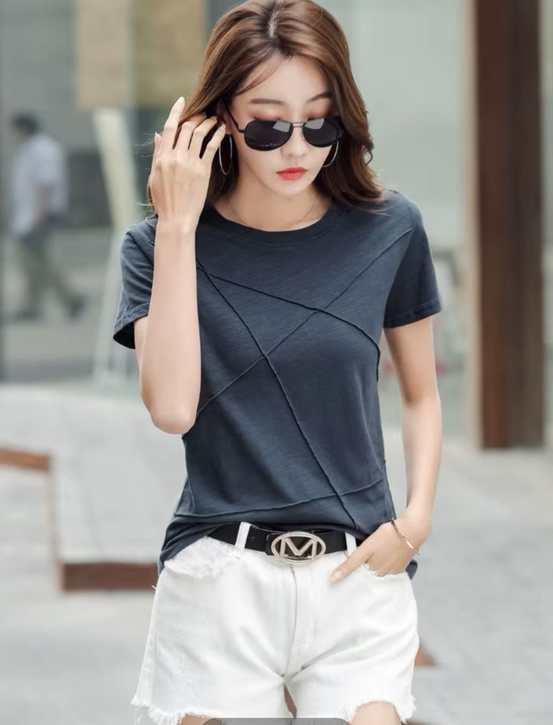 Woman wearing a dark blue top and white shorts with sunglasses, standing outdoors.