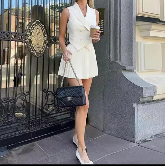 Woman in a white dress holding a coffee cup and black handbag standing in front of a building entrance.