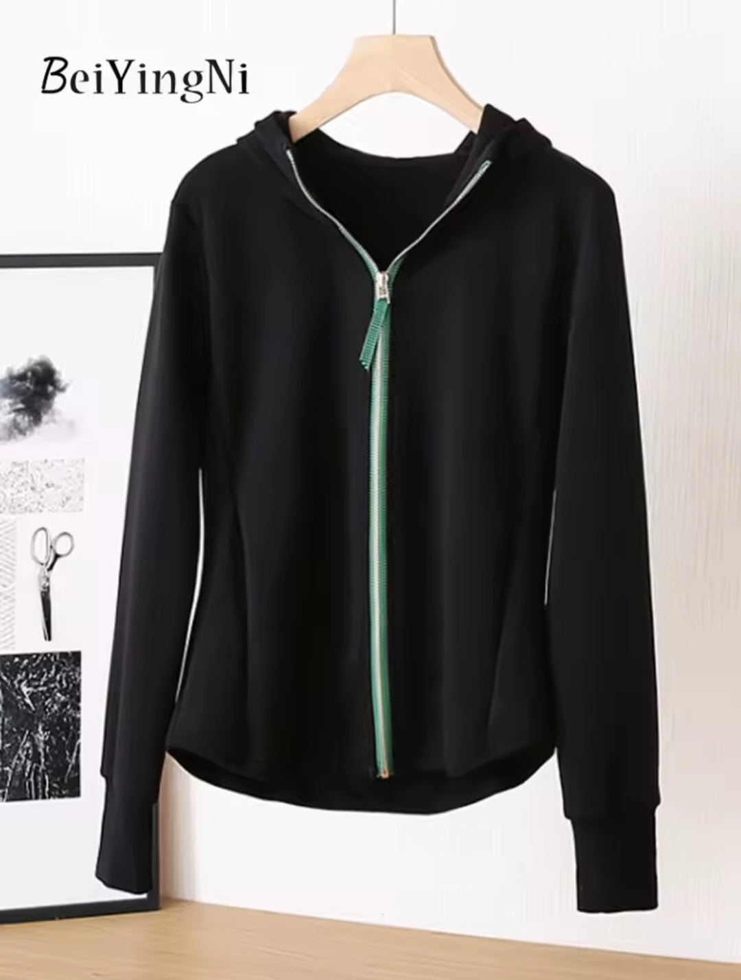Black hoodie with a zipper on a hanger against a white wall, brand 'BeiYingNi' visible.