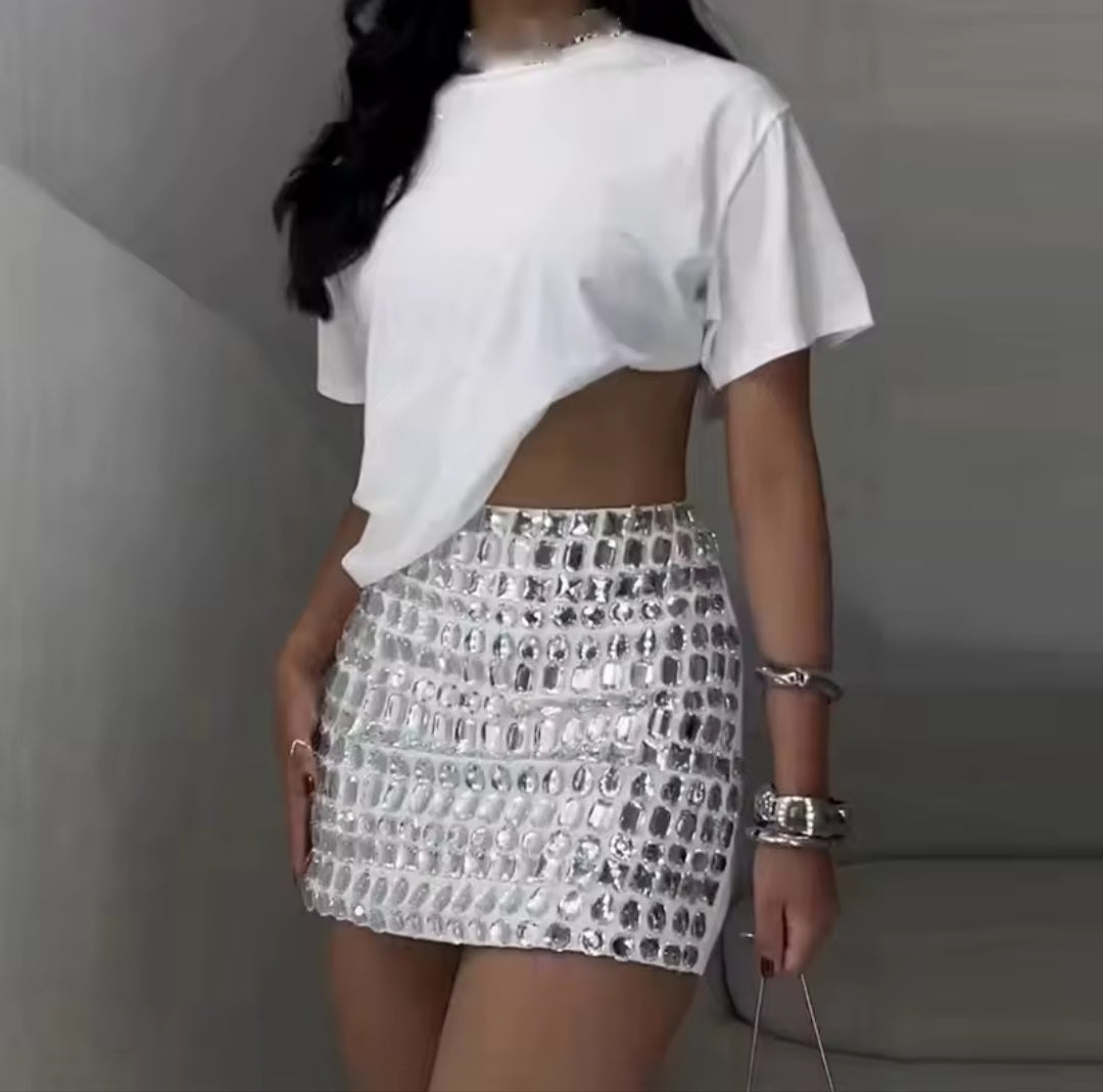 Person wearing a white open-back top and silver sequin skirt against a neutral background