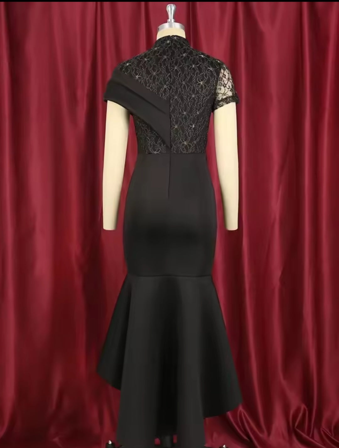 Black dress with lace detailing on a mannequin against a red curtain background
