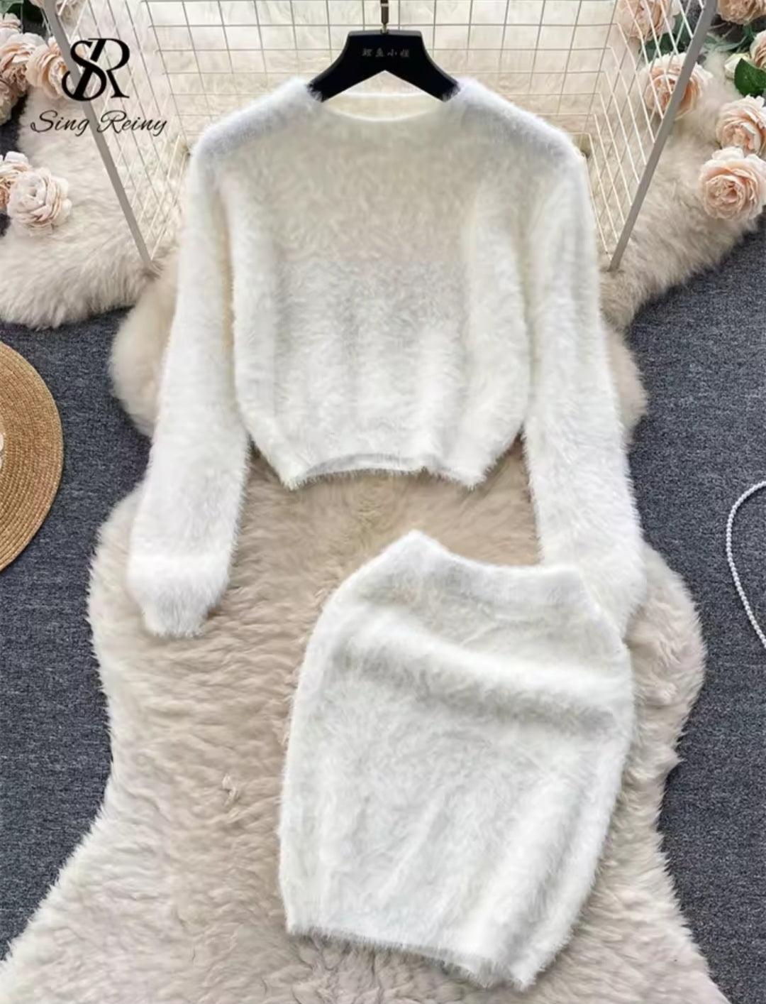 White fluffy sweater and skirt set on a hanger with floral decorations in the background.
