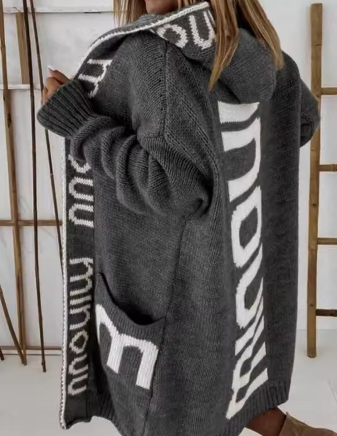 Gray cardigan with white text pattern worn by a person indoors.