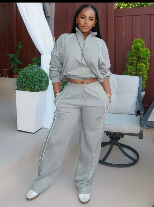 Woman in gray tracksuit standing outdoors with plants and furniture in the background