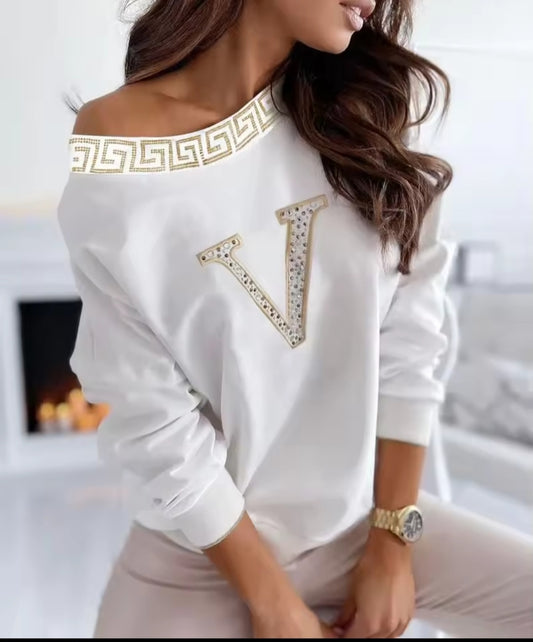 Woman wearing a white blouse with gold detailing in a blurred indoor setting