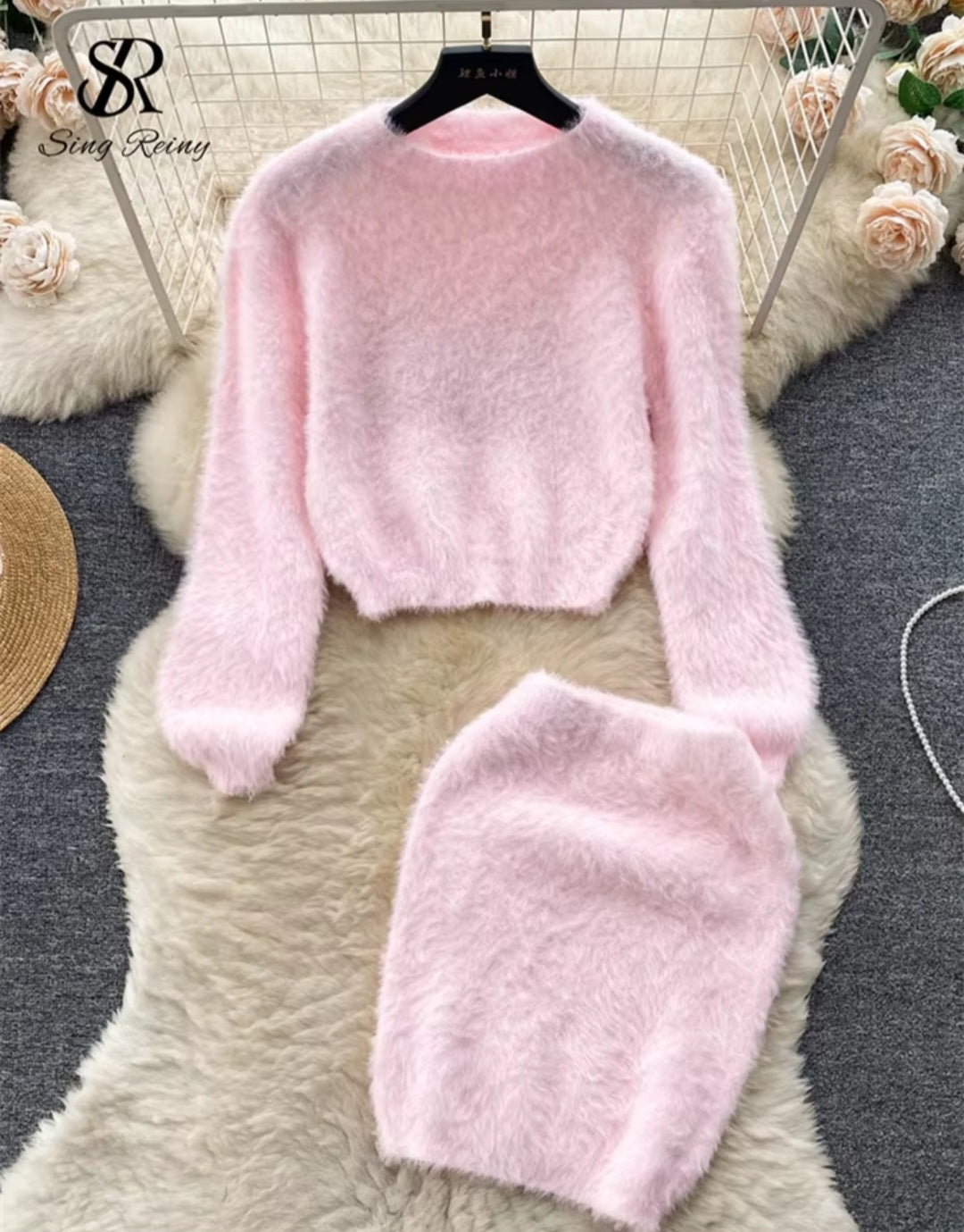 Pink fluffy sweater and skirt set on a textured surface with flowers in the background