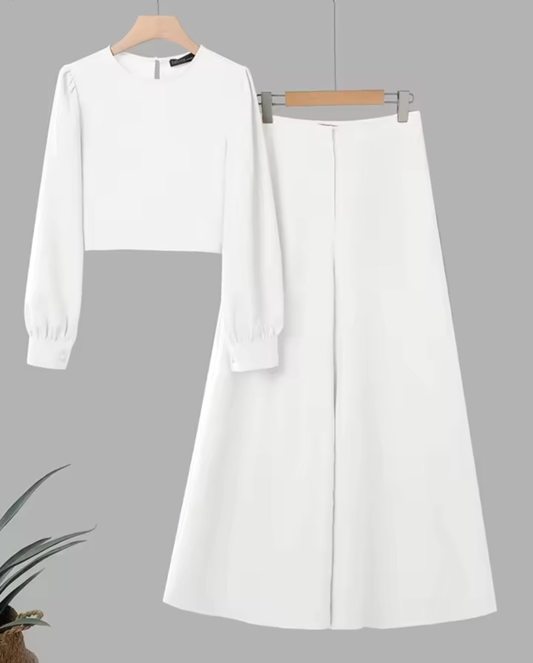 White long-sleeve top and skirt set on hangers against a gray background