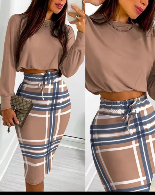 Woman wearing a brown long-sleeve top and plaid skirt with a white background.