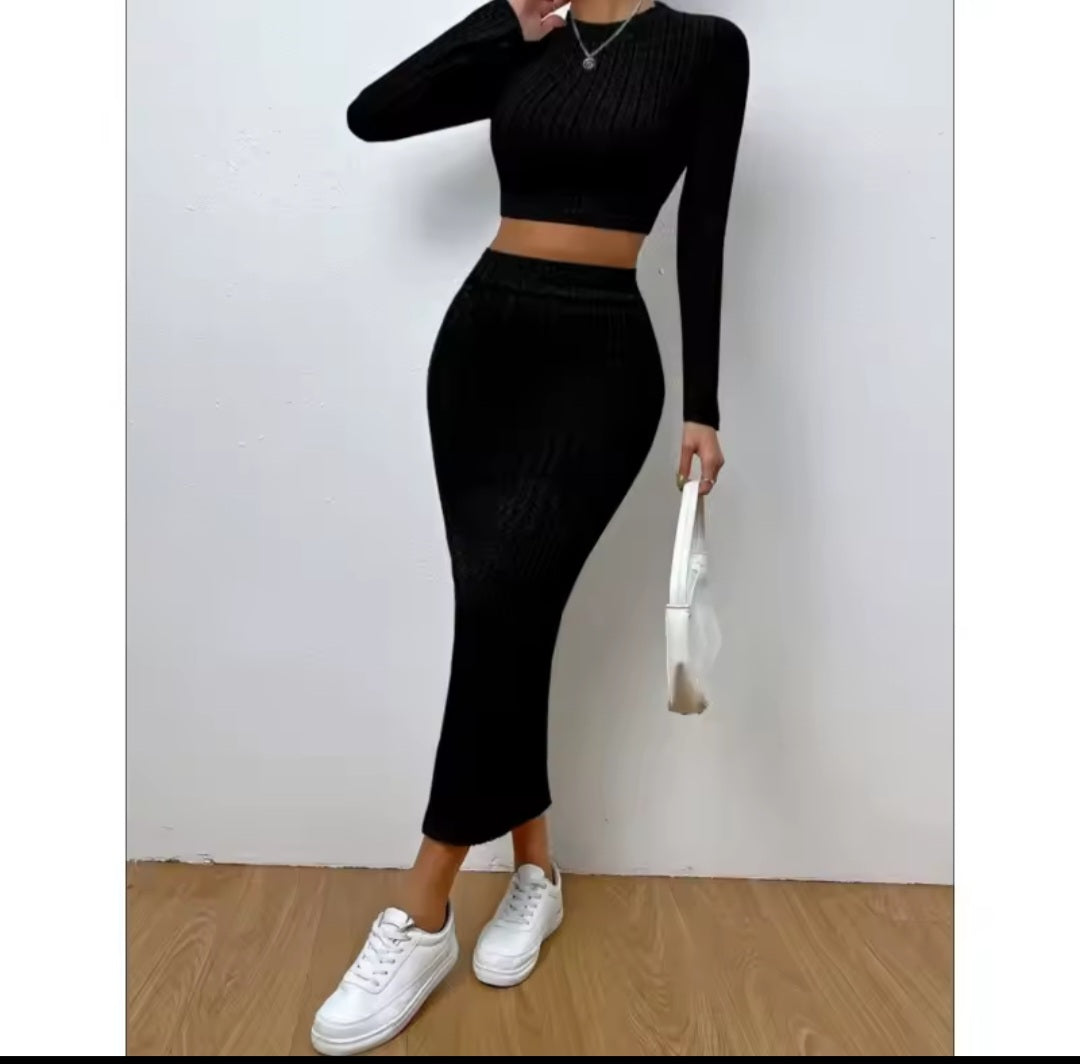 Person wearing a black long-sleeve top and black skirt with white sneakers on a plain background