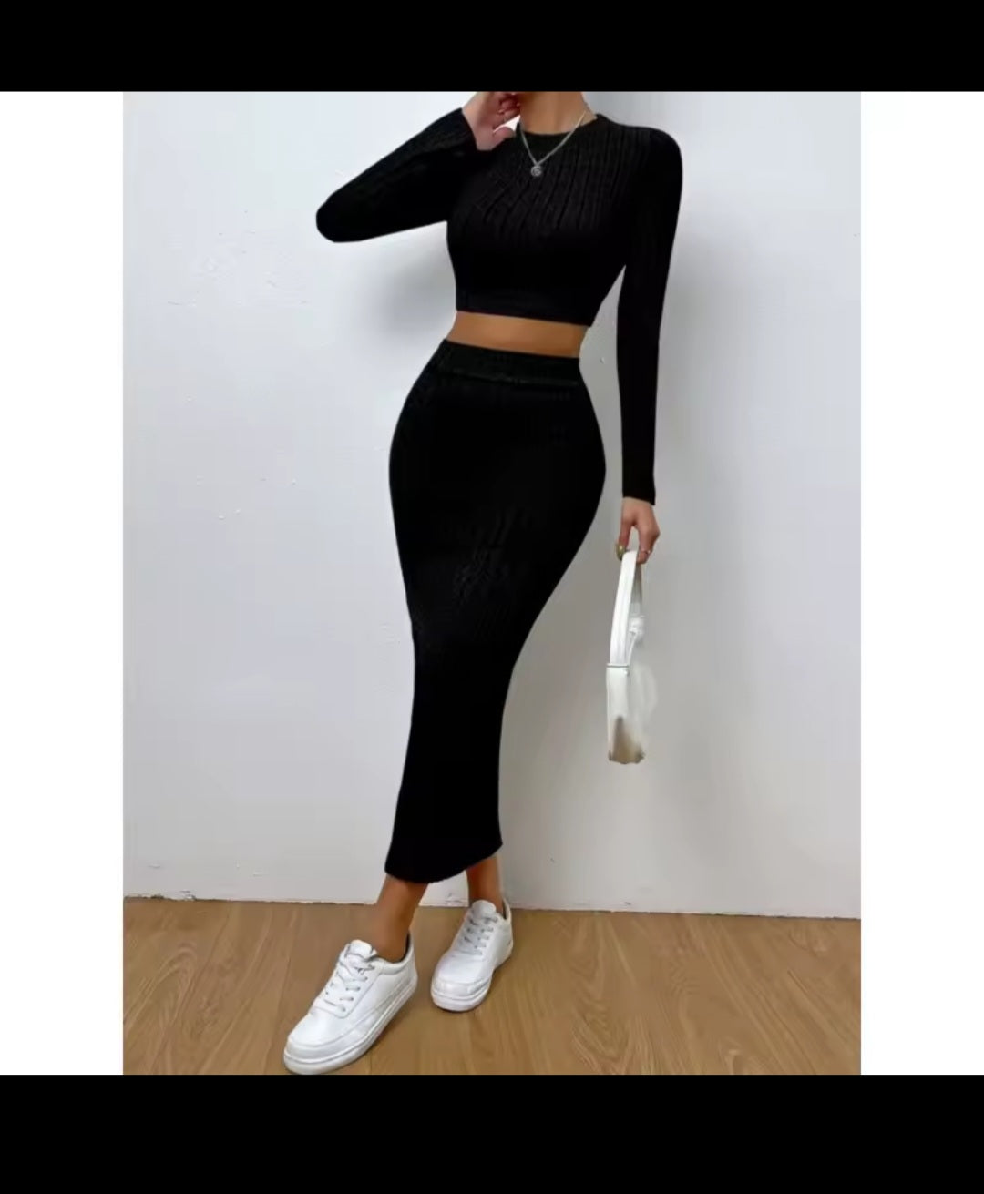 Person wearing a black long-sleeve top and high-waisted pants with white sneakers on a plain background