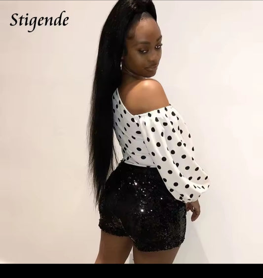 Woman wearing a polka dot top and black sequin shorts against a plain background